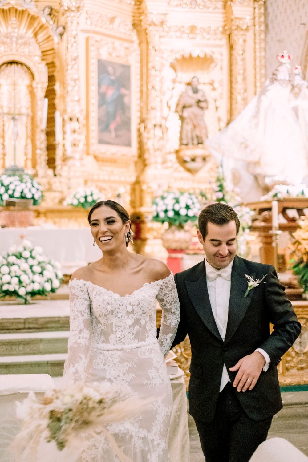 A joyful wedding ceremony exit in an ornate church decorated with white floral arrangements.