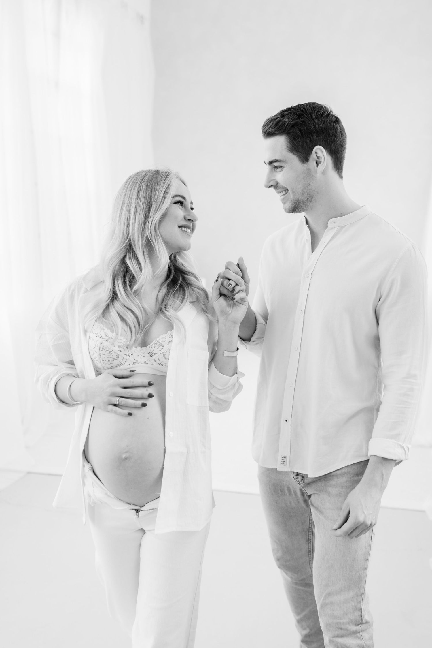 A light and airy series of romantic maternity portraits showing a couple in white clothing against a bright background.