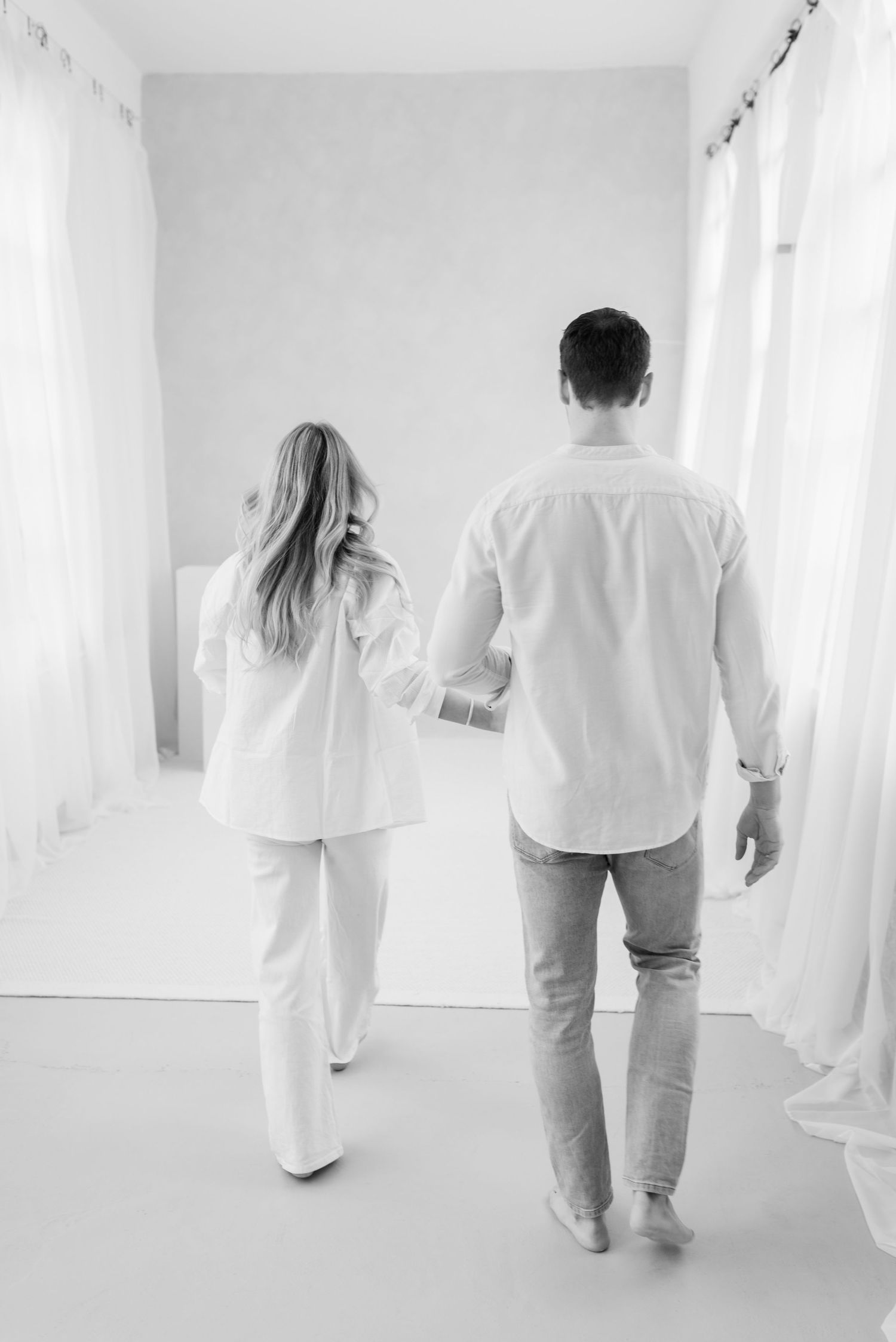 People in white clothing walk through a bright minimalist hallway.