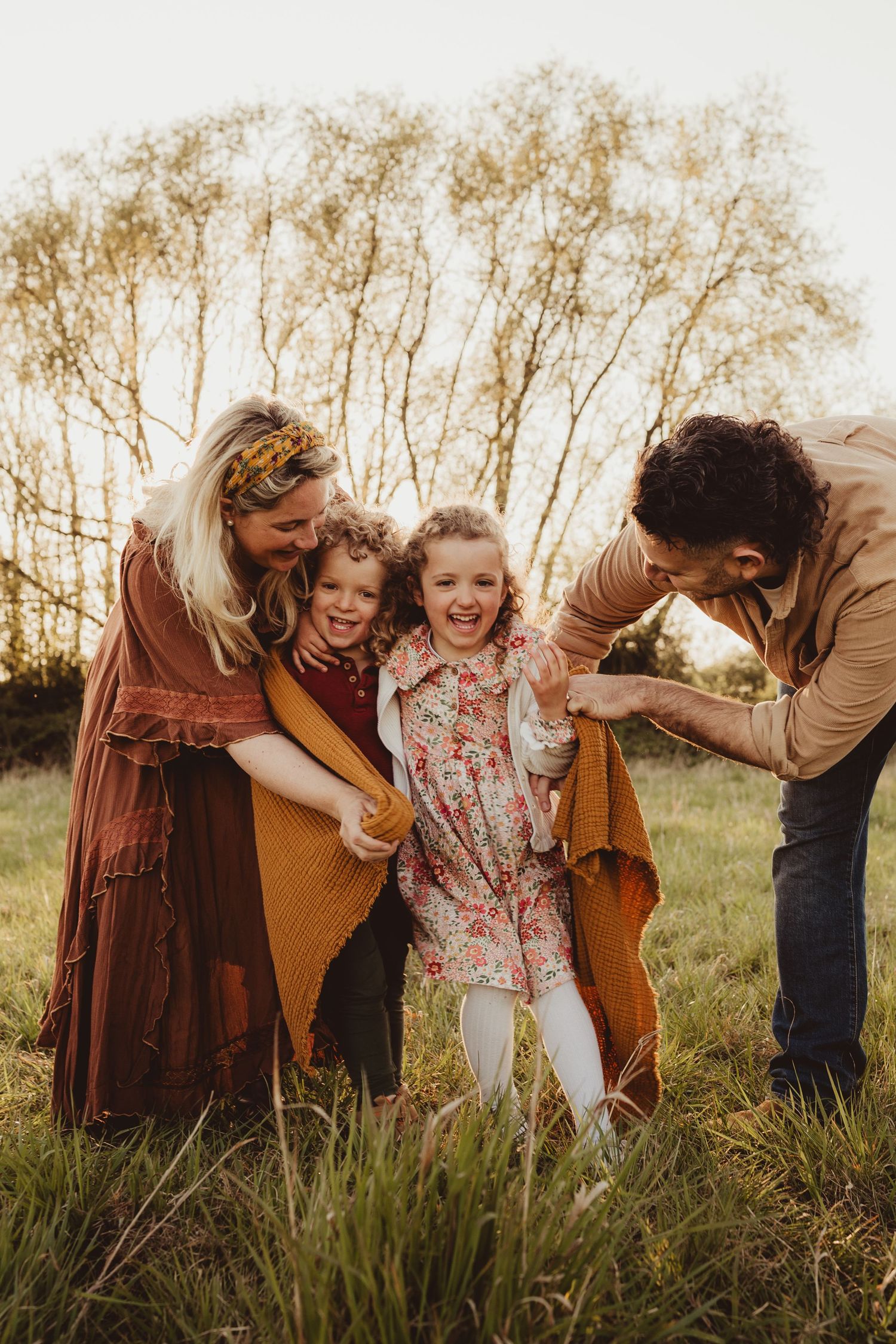 A group in warm earth-toned clothing poses together in a sunlit autumn field at golden hour.
