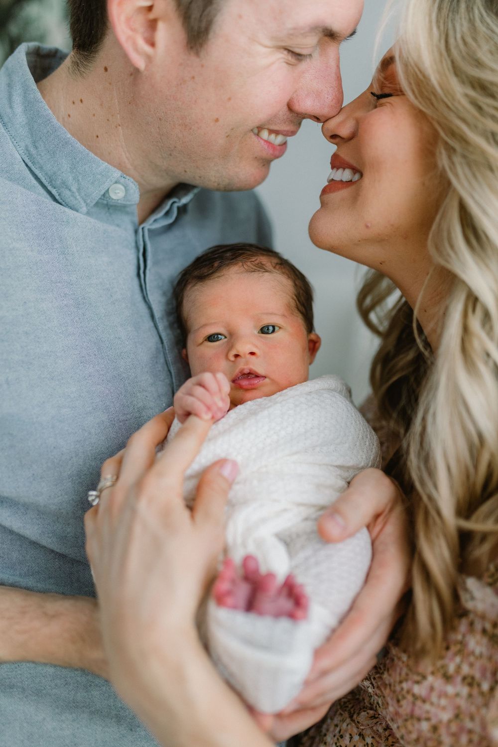 Intimate family portrait shows parents sharing tender moment with their newborn.