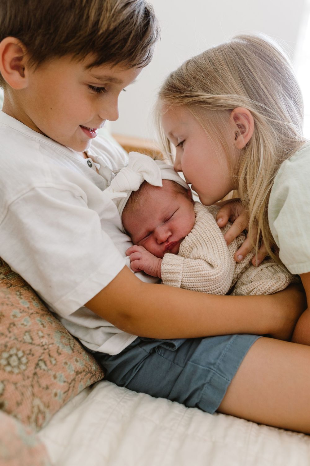 Siblings share sweet moment with their new baby brother wrapped in knit blanket.