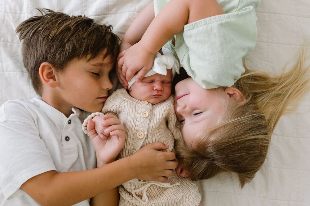 A sweet candid moment of sibling bonding with a newborn baby as the family lies together on a bed.
