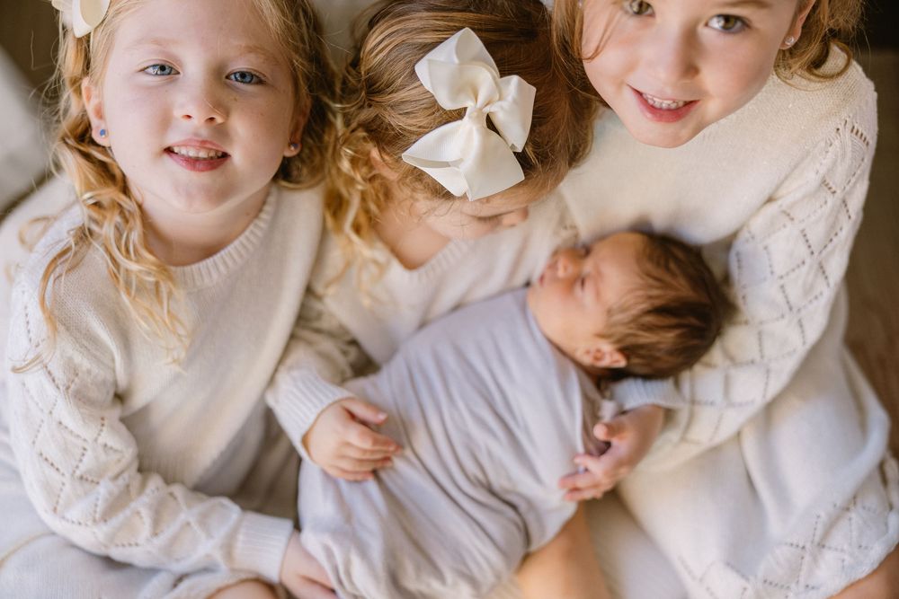 Children in white sweaters gather close to admire their new baby sibling.
