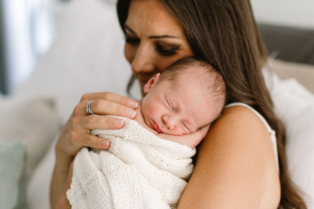 Tender moment between parent and sleeping newborn wrapped in white knit blanket.
