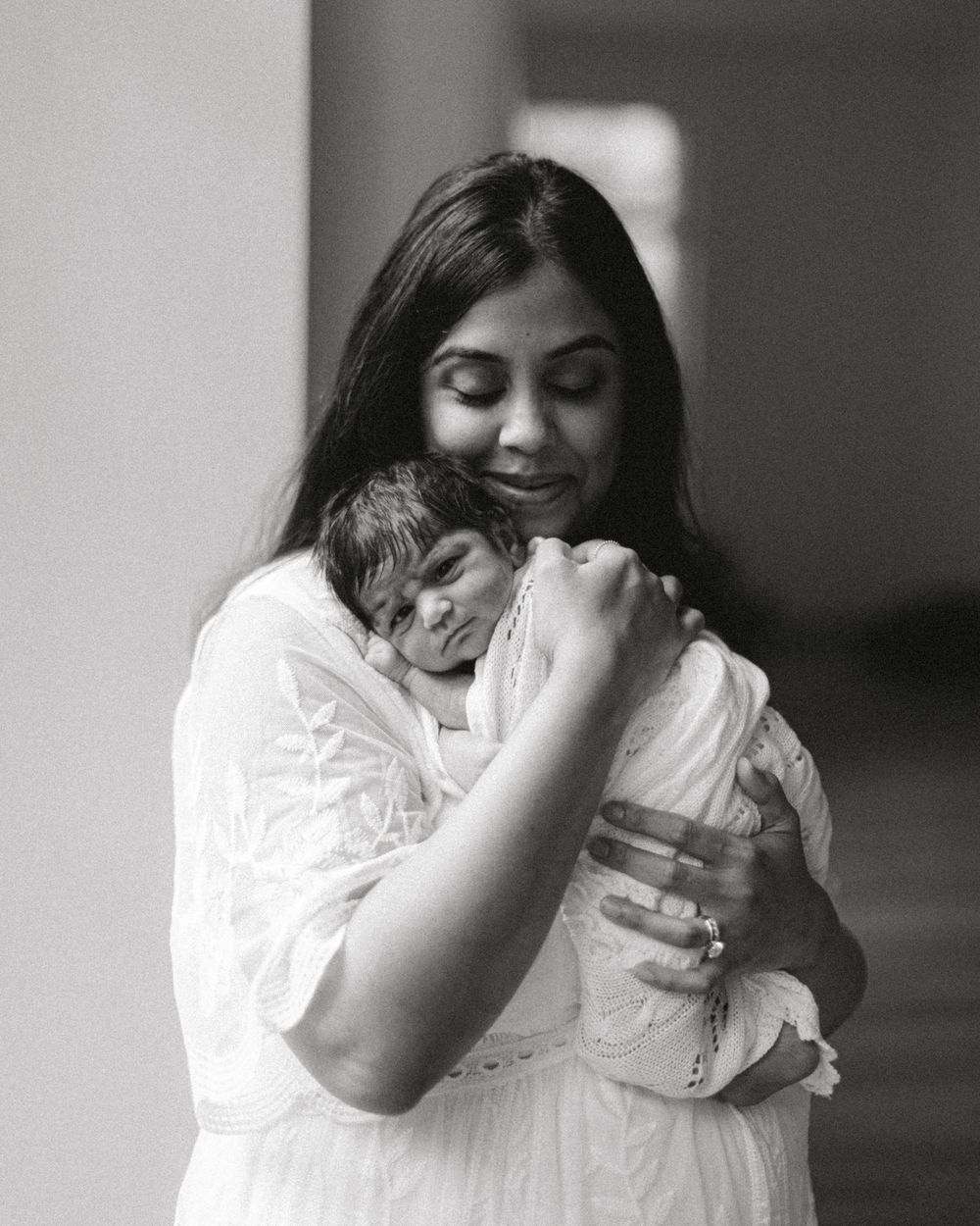 Black and white portrait of mother and baby embracing in tender moment.