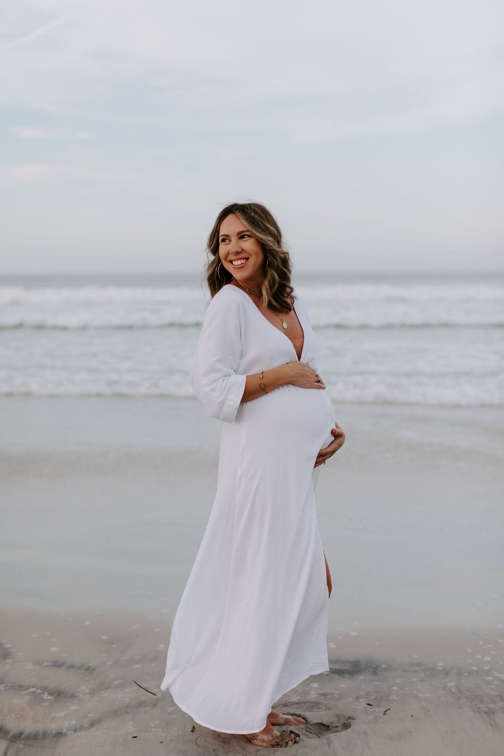 Person in flowing white dress twirling joyfully on beach.