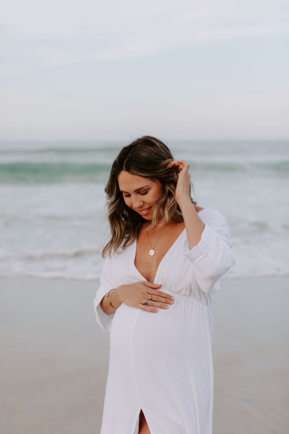 Woman in white beach dress posing against ocean backdrop.