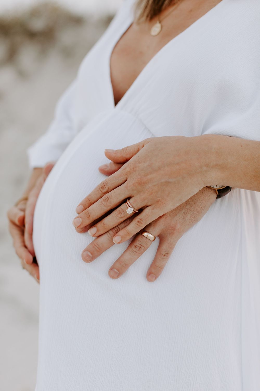 Close-up of hands resting on a pregnant belly showing an engagement ring.