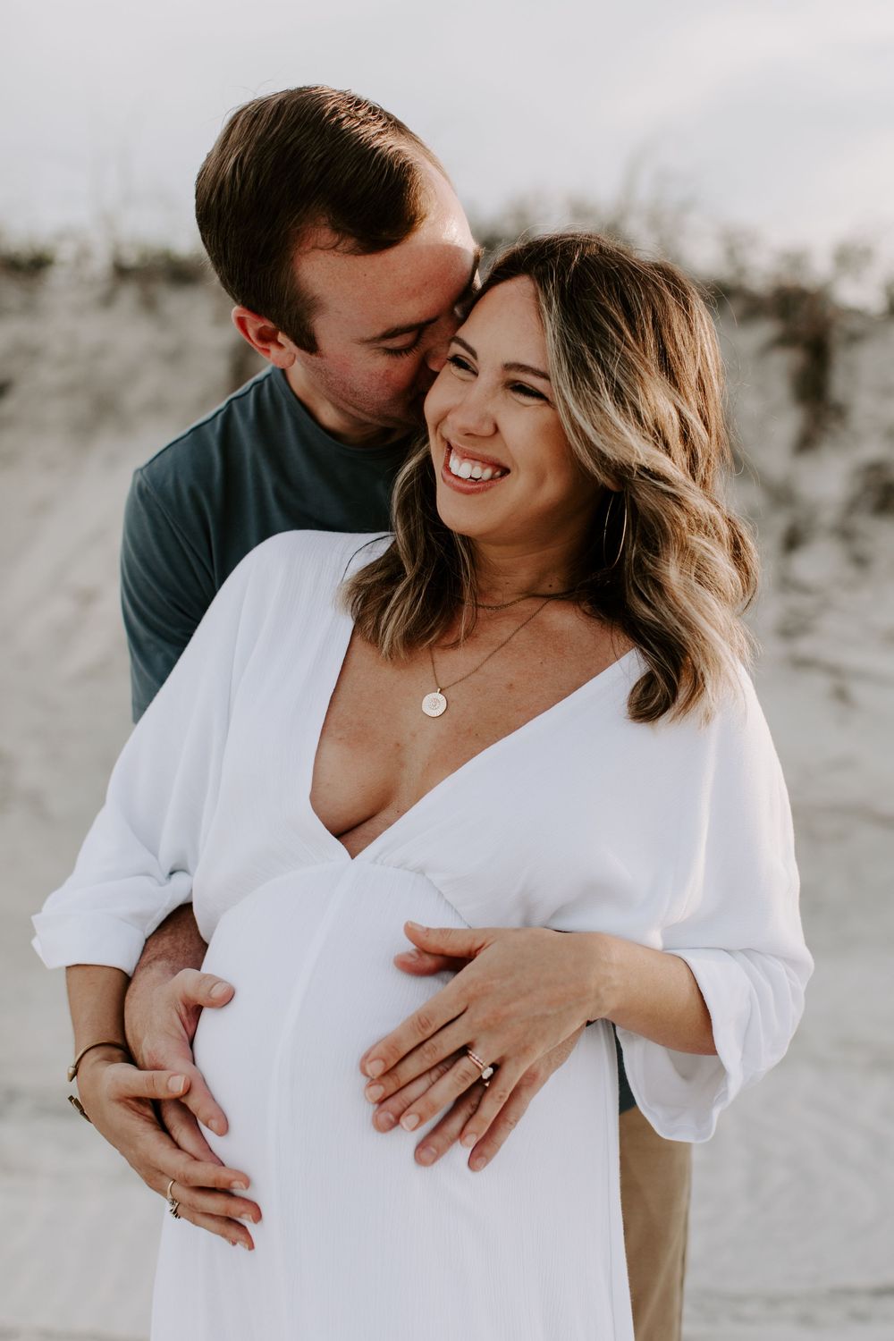 Joyful maternity beach photo with couple embracing and laughing together.