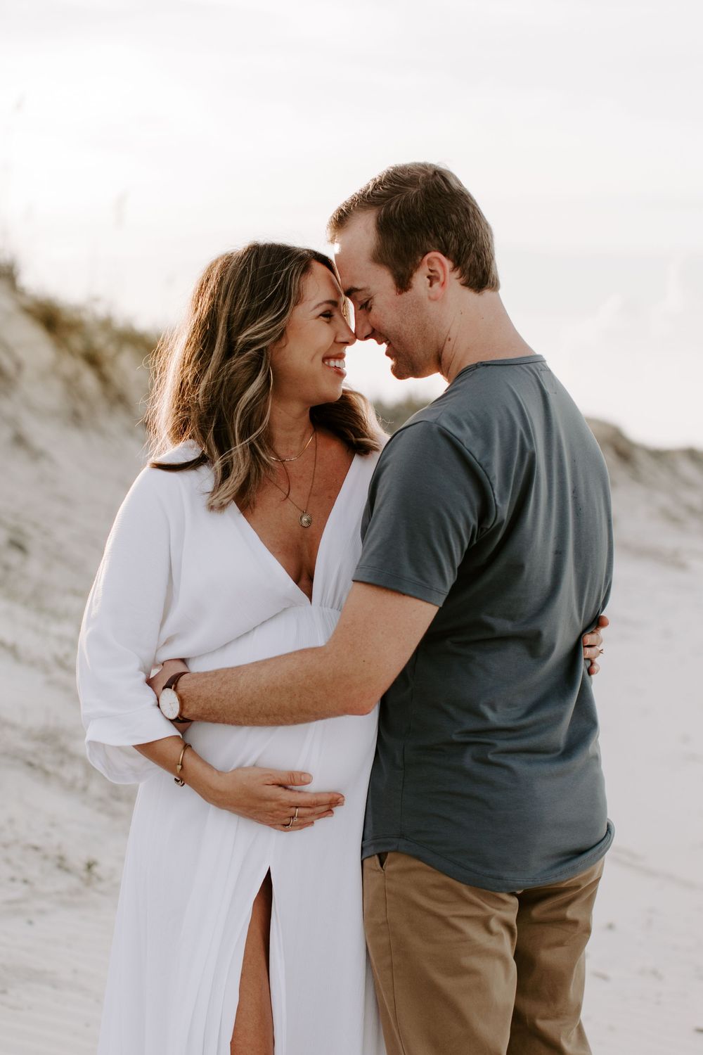 Romantic maternity portrait of couple in casual attire sharing an intimate moment on the beach.