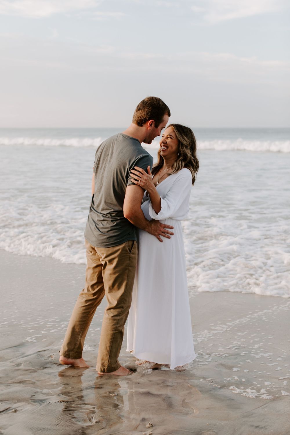 A romantic couple shares a joyful moment together on a misty beach shore.