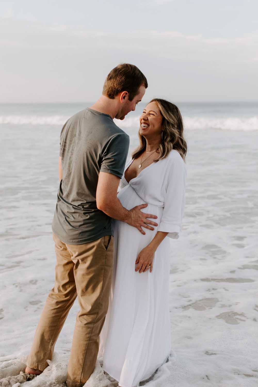 Playful beach maternity photo capturing couple's laughter and joy by the ocean.