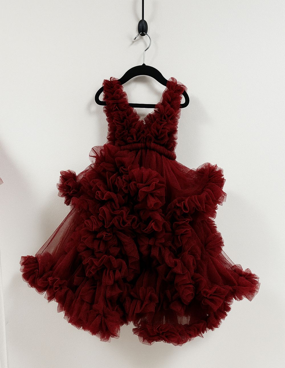 Deep burgundy red tulle ruffle dress with dramatic layered skirt and fitted bodice hanging on black hanger.
