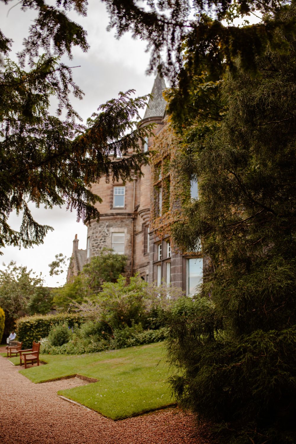 A majestic Scottish castle with stone facade surrounded by lush gardens and trees.