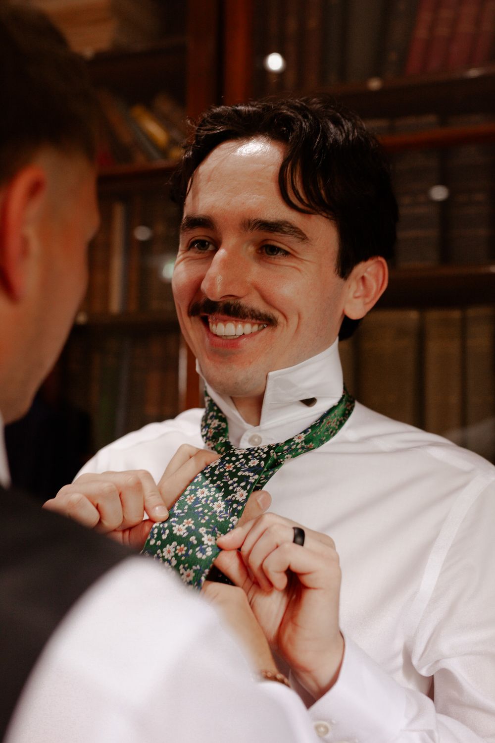 Person having a floral patterned tie adjusted during wedding preparations.