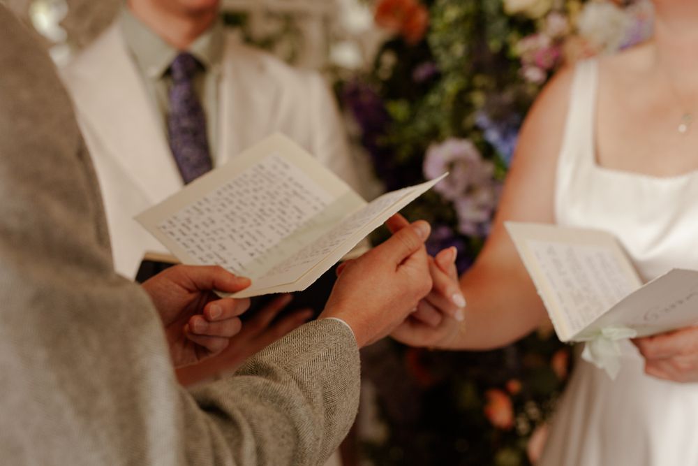 Couple exchanging vows while holding ceremony papers during wedding.