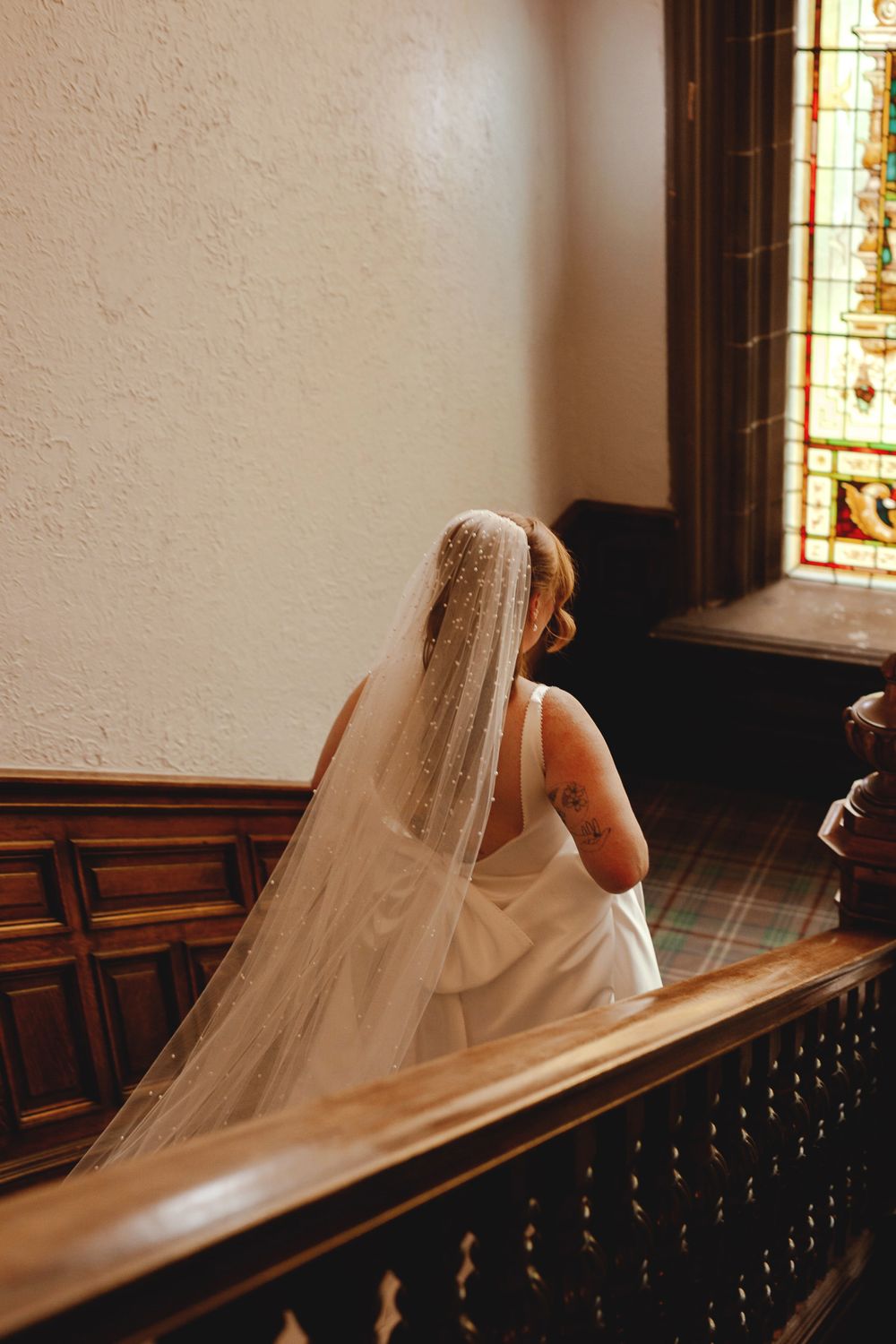 Wedding dress and veil detail on historic wooden staircase.