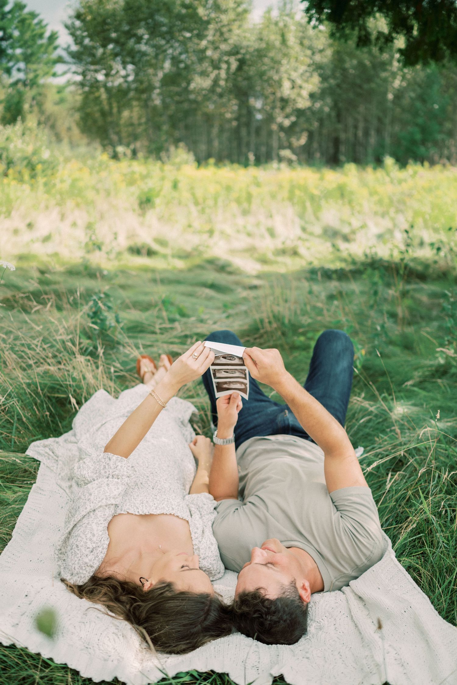 Couple lying on blanket in meadow looking at phone together.