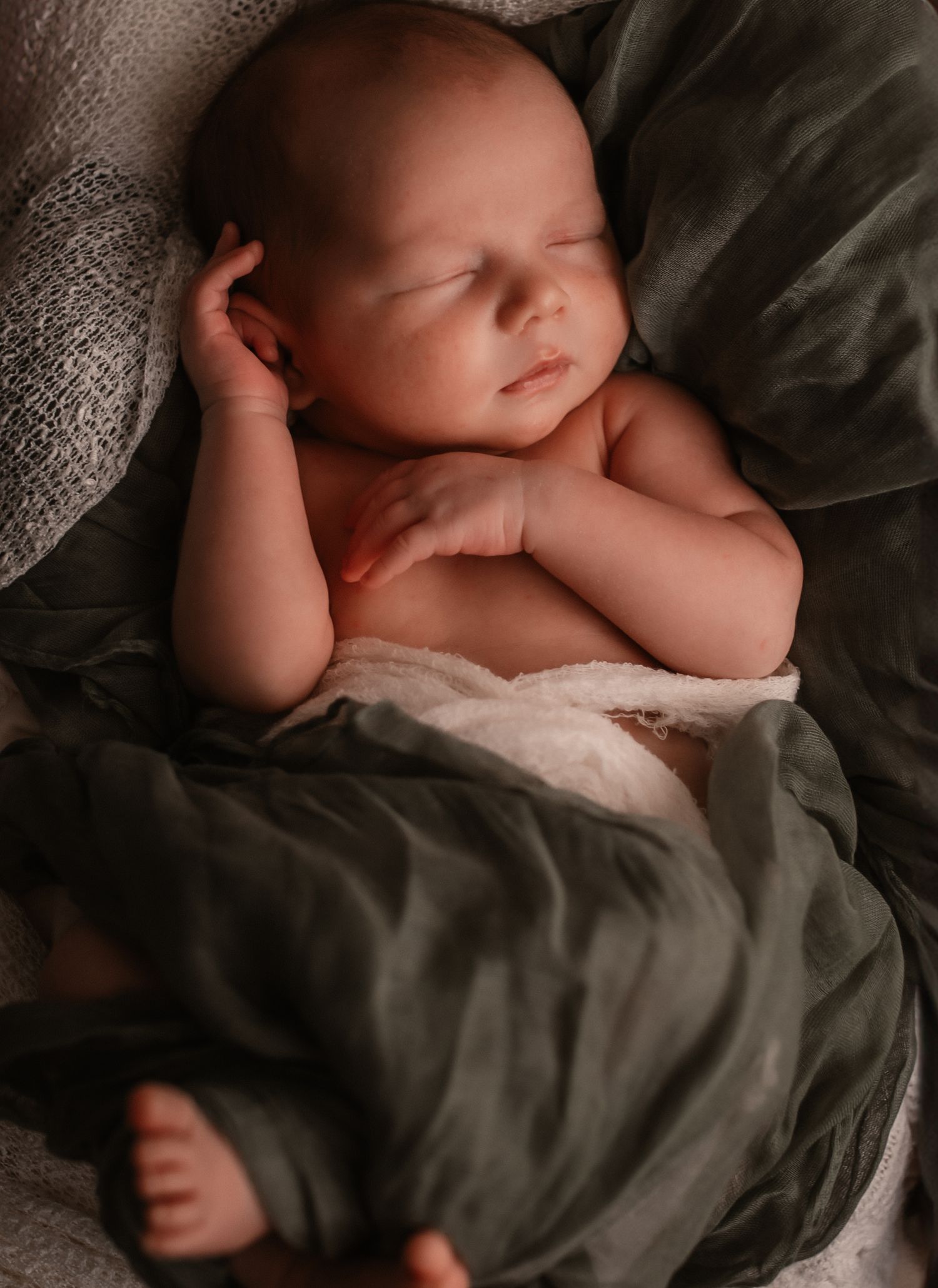 A sleeping newborn baby lies peacefully on soft gray textured bedding in a moody artistic portrait.