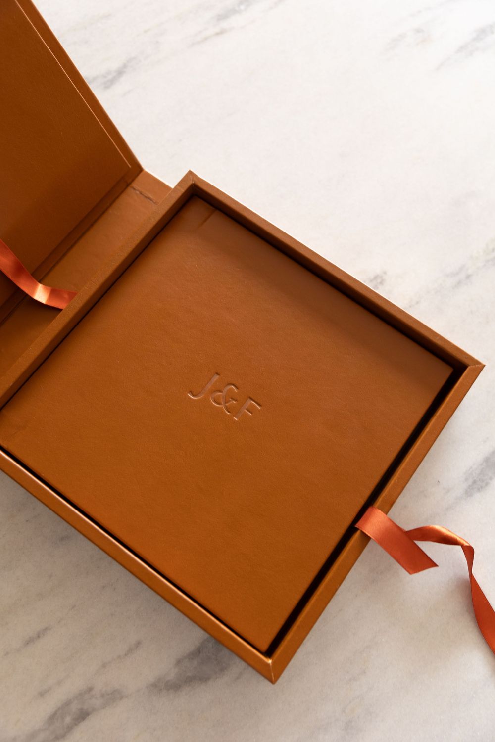 Leather-bound presentation box with embossed text and orange ribbon detail on marble surface.