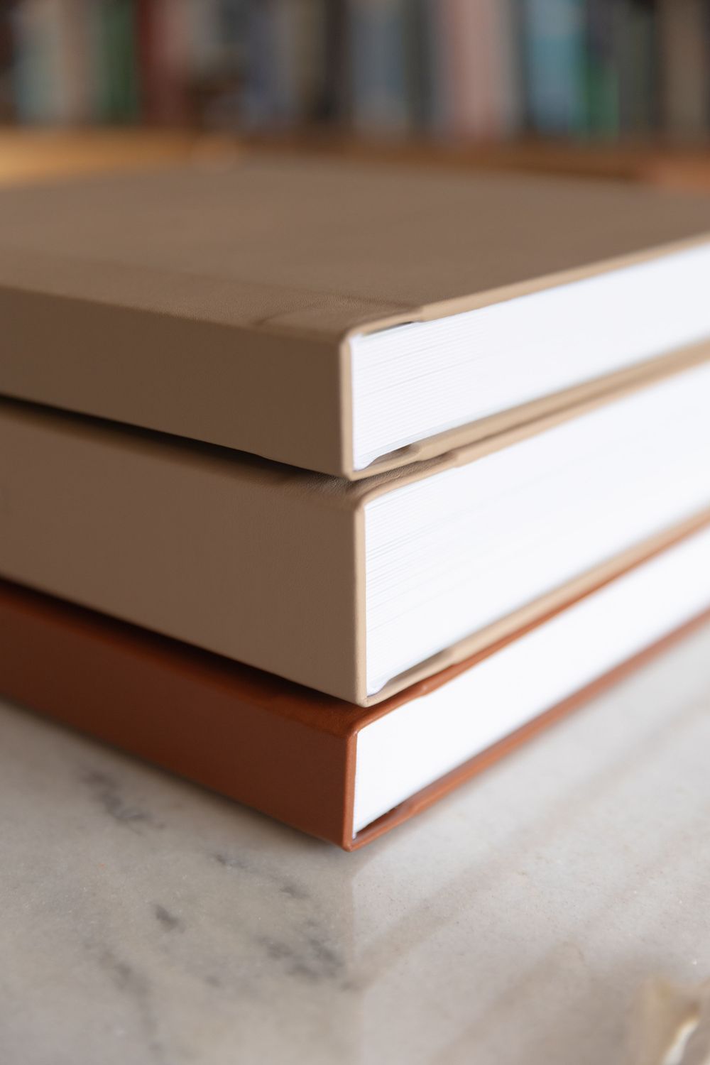 Stack of three books showing white pages and brown covers on marble surface.