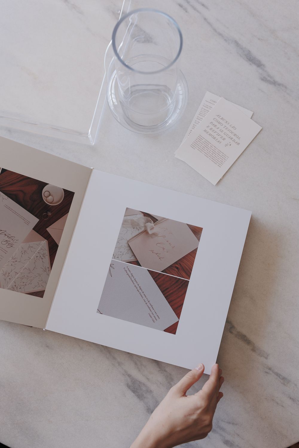 Overhead view of photo album on marble surface with glass and invitation details.