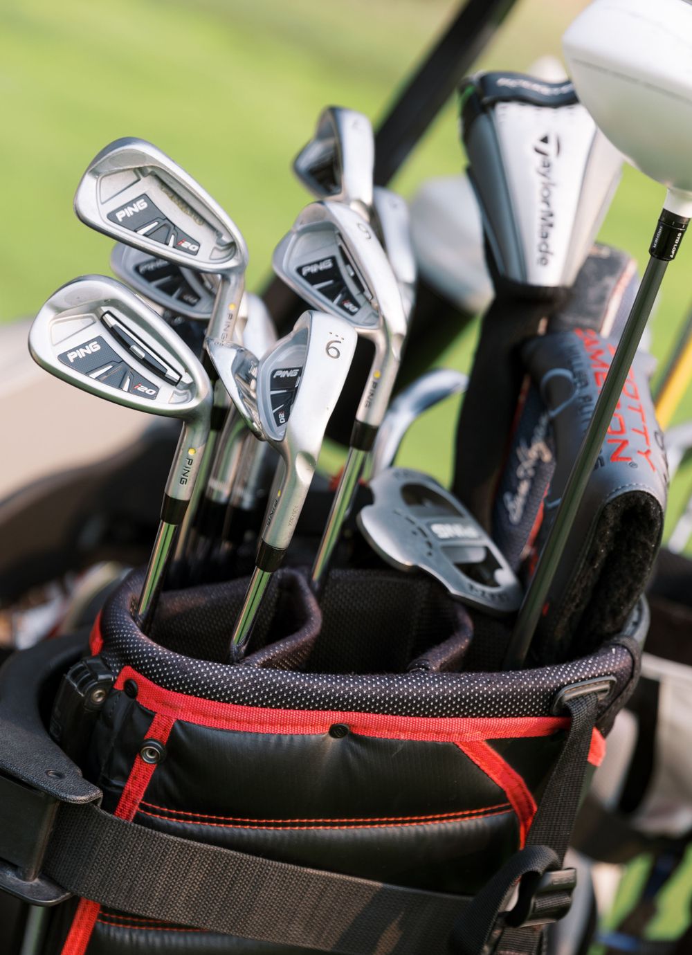 A set of TaylorMade golf clubs with irons and woods arranged in a black and red golf bag on a golf course.