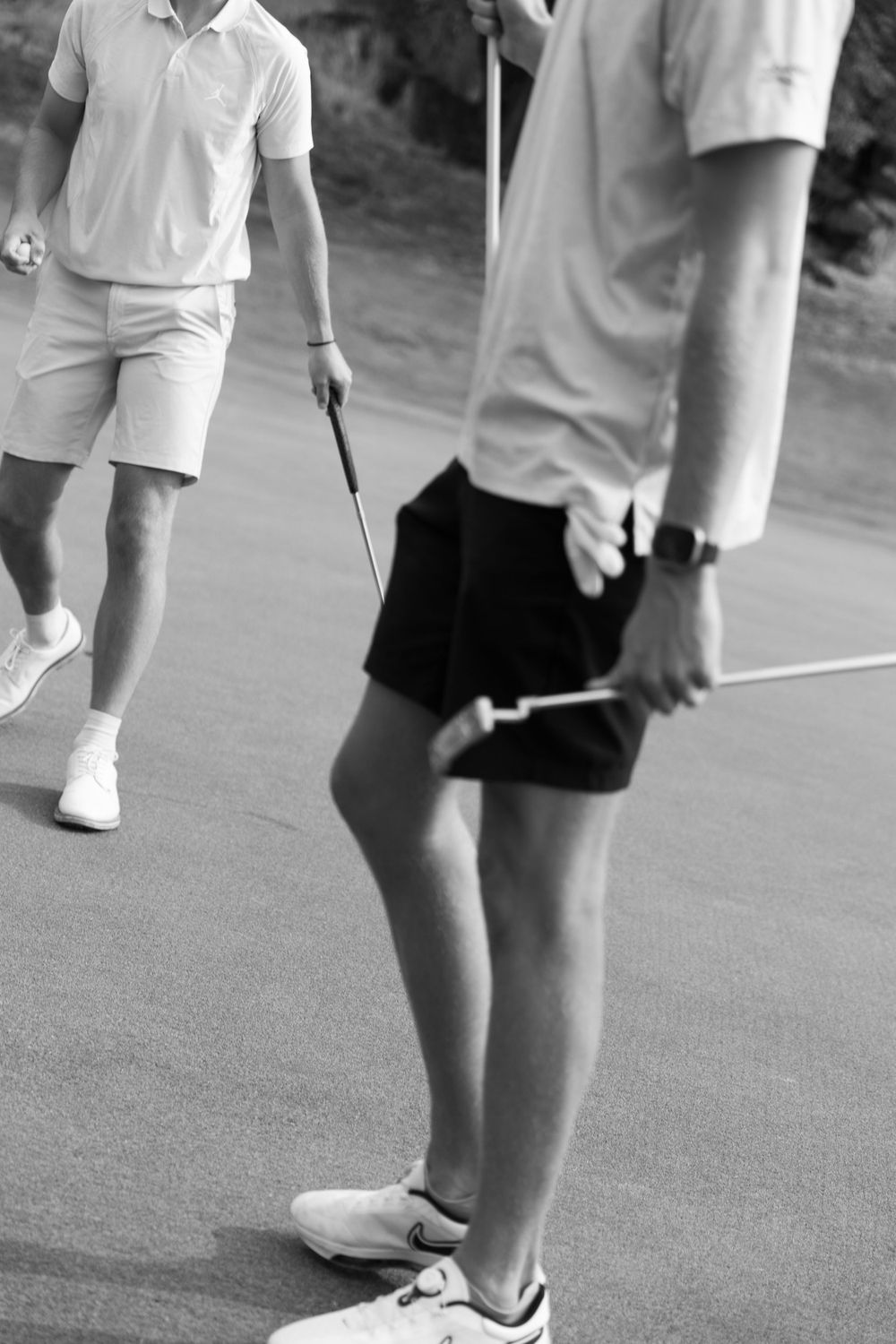 Black and white photo of golfers in casual attire with white polo shirts and shorts standing on a golf course.