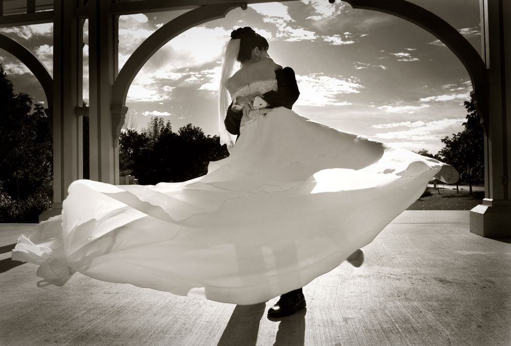 A silhouetted couple dancing at sunset, with the bride's white dress flowing dramatically in motion.