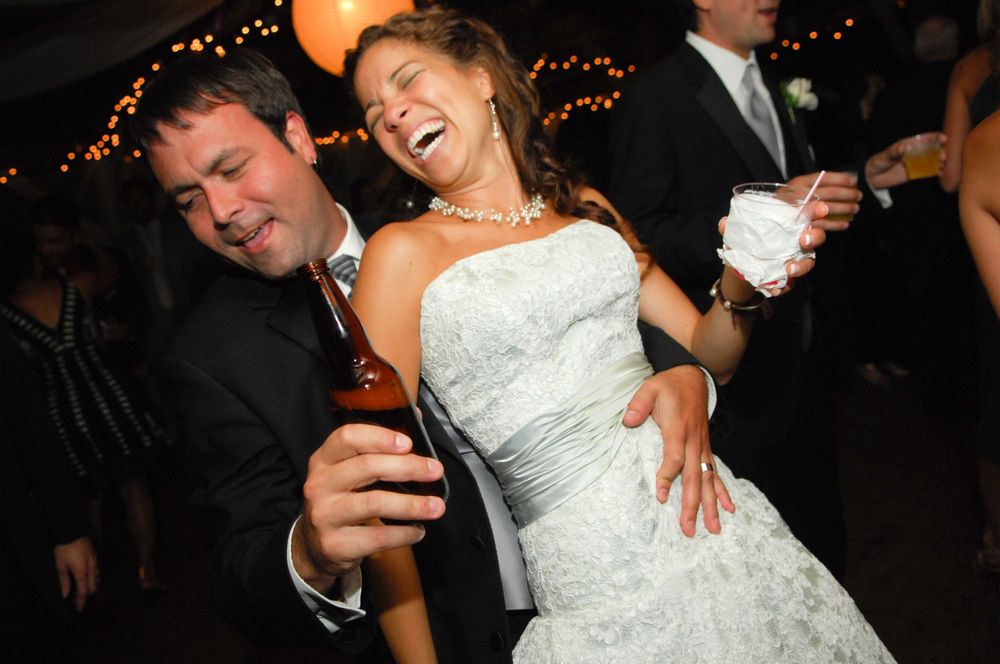 Couple dancing and laughing at a reception with string lights in the background.