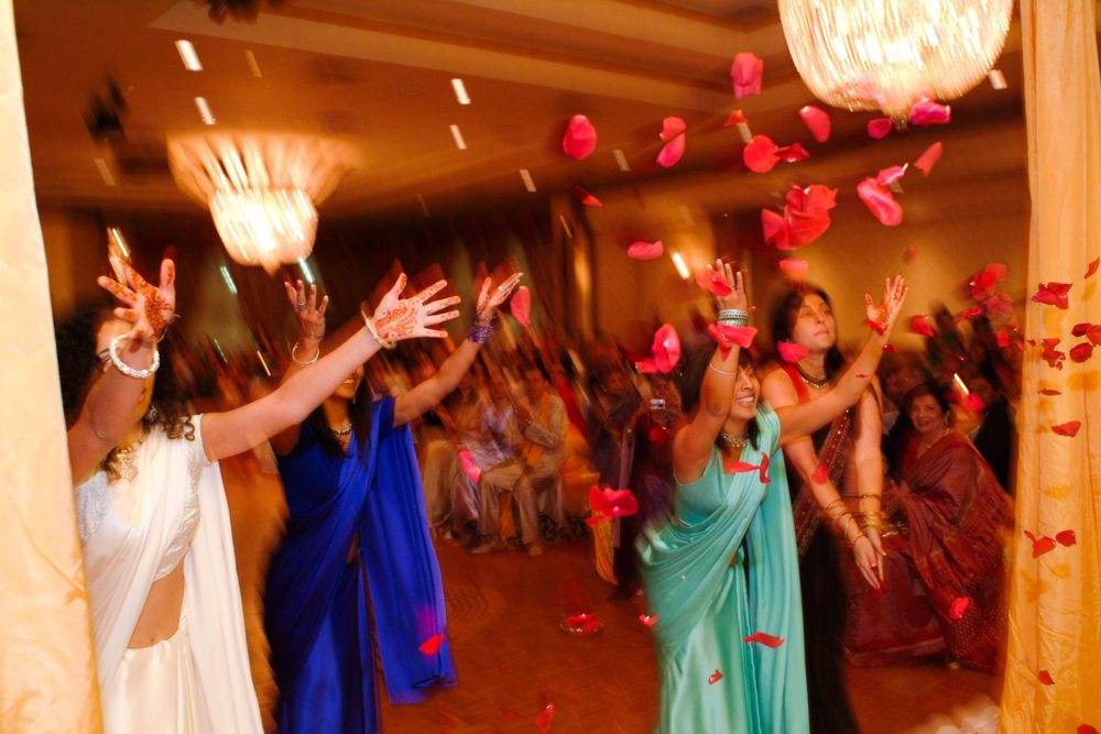 Wedding party guests dance and celebrate with raised arms amidst colorful decorations and lighting.