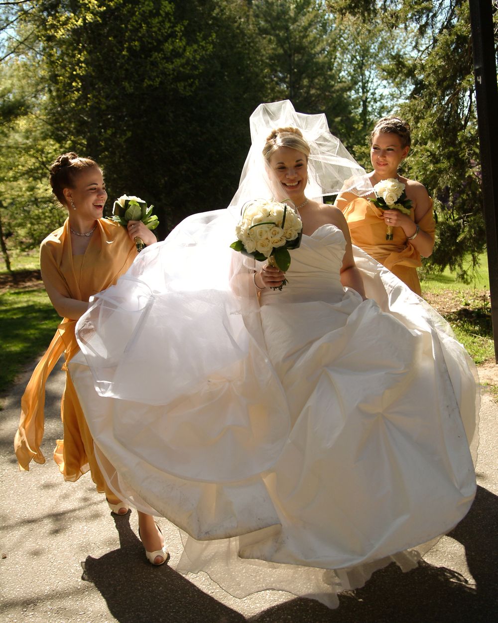 Wedding party poses under stone archway in front of historic building.