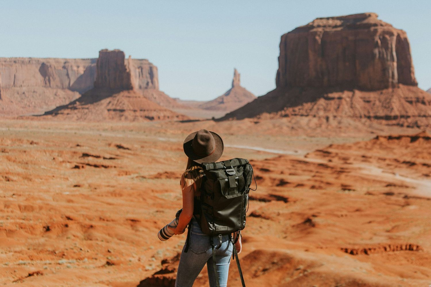 Hiker with backpack overlooking Monument Valley's iconic red rock formations.