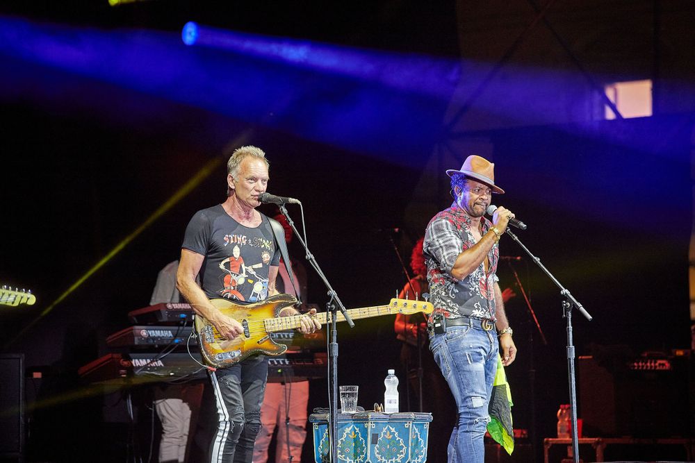 Musicians performing on stage with guitars under blue spotlight.