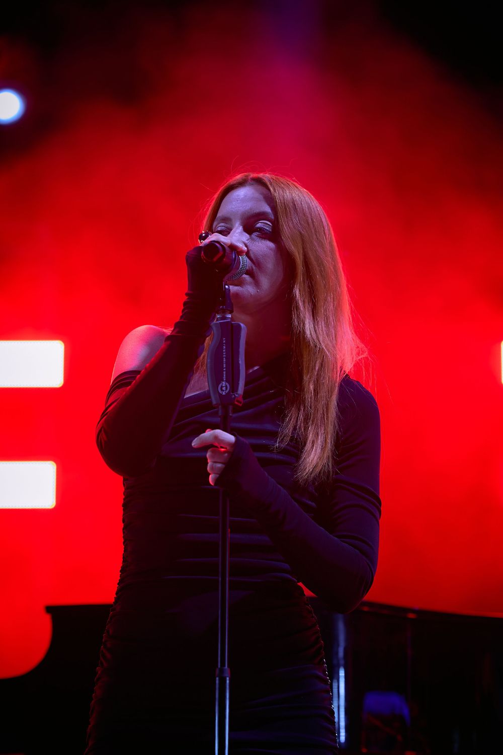 Concert performance on stage with dramatic red lighting and atmospheric smoke effects.