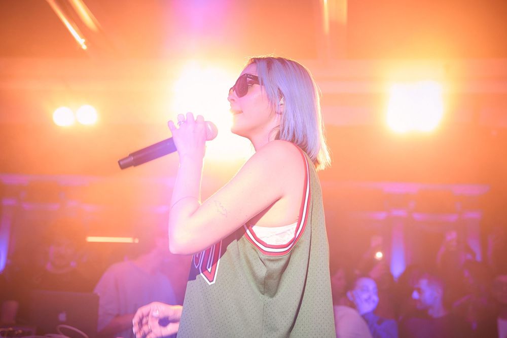 Performer singing on stage with dramatic orange backlighting during concert performance.