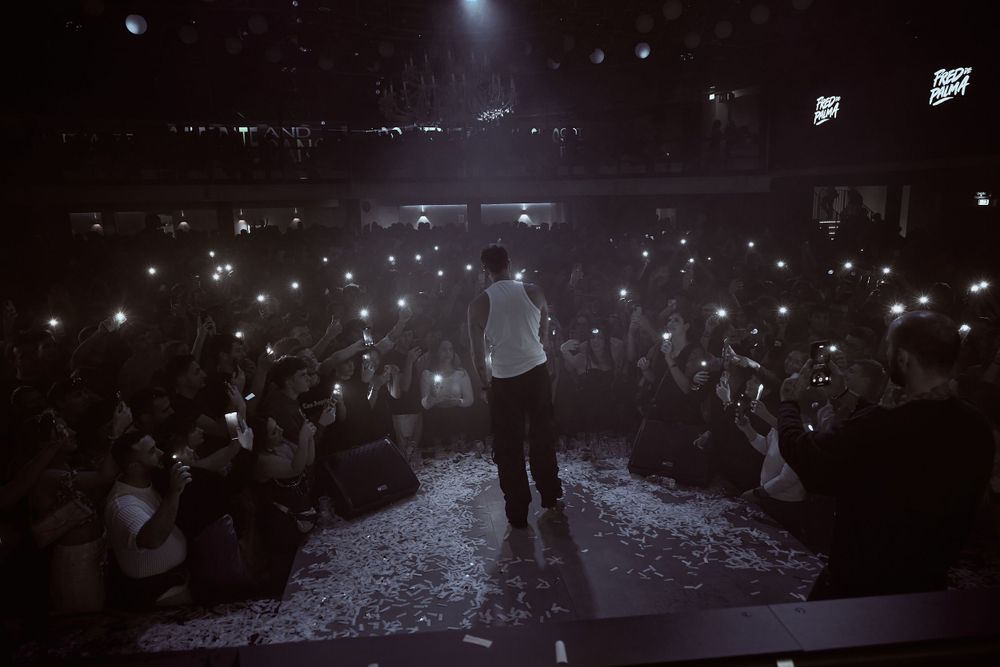Silhouetted figure on stage performing to crowd holding glowing phones at concert venue.
