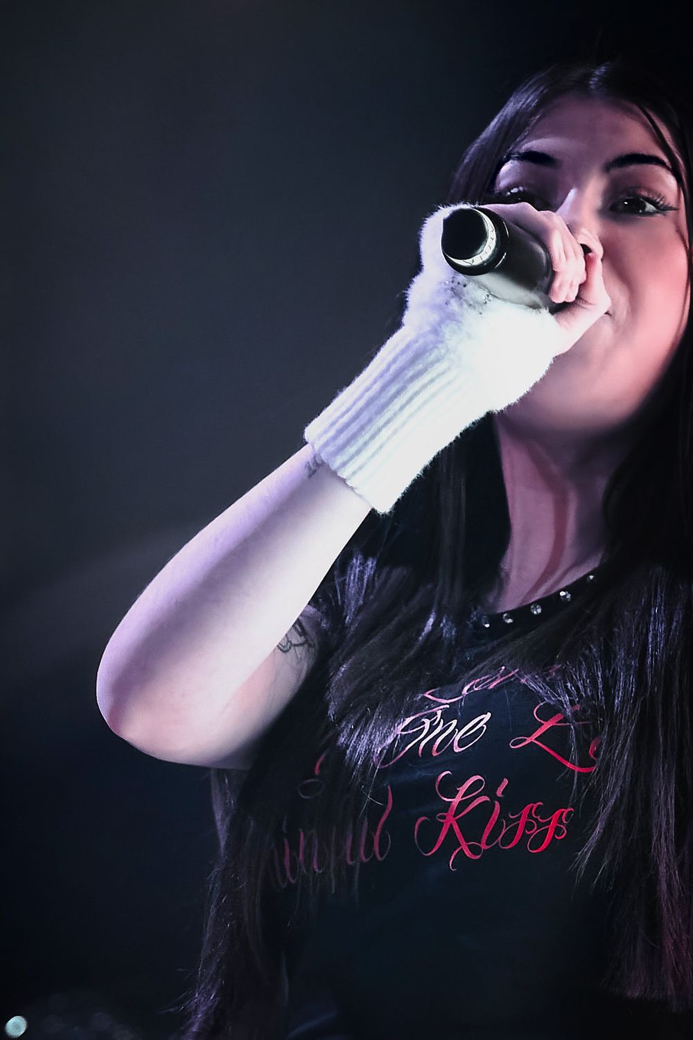 Female performer in black t-shirt sings into microphone during concert performance.