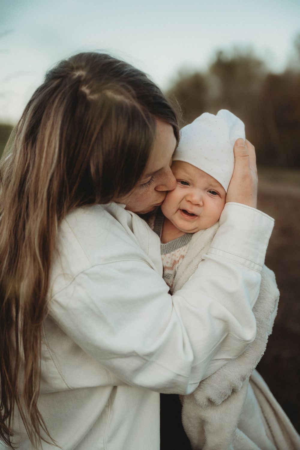 Tender moment between parent and baby bundled in white clothing outdoors.