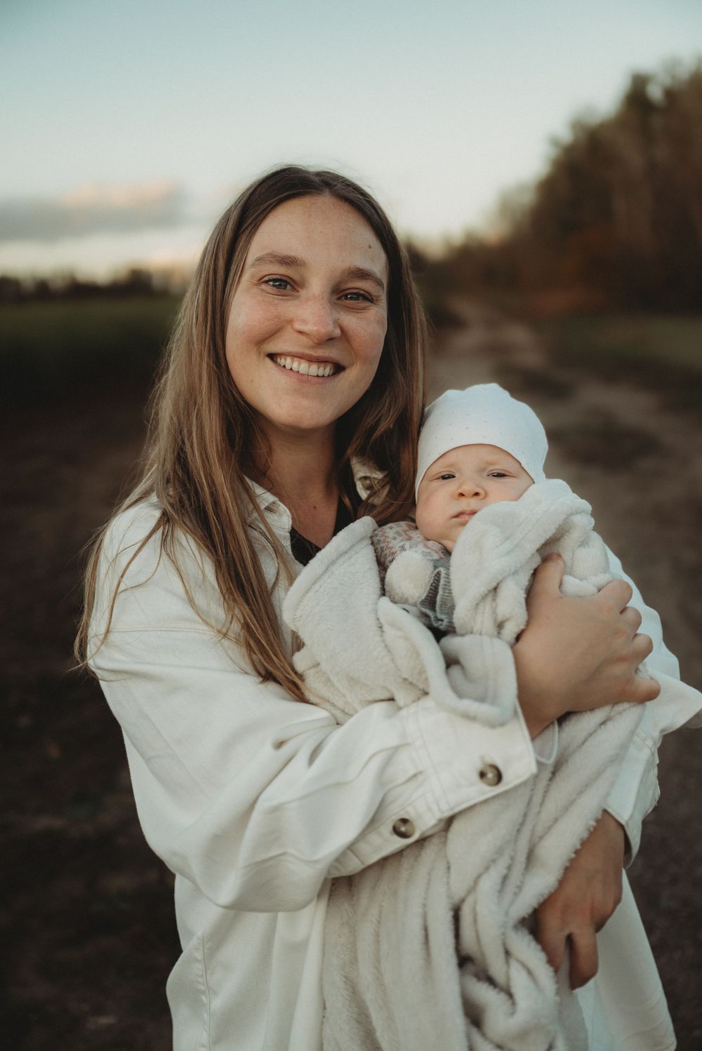 Parent in white coat holding baby wrapped in cozy blankets outdoors.