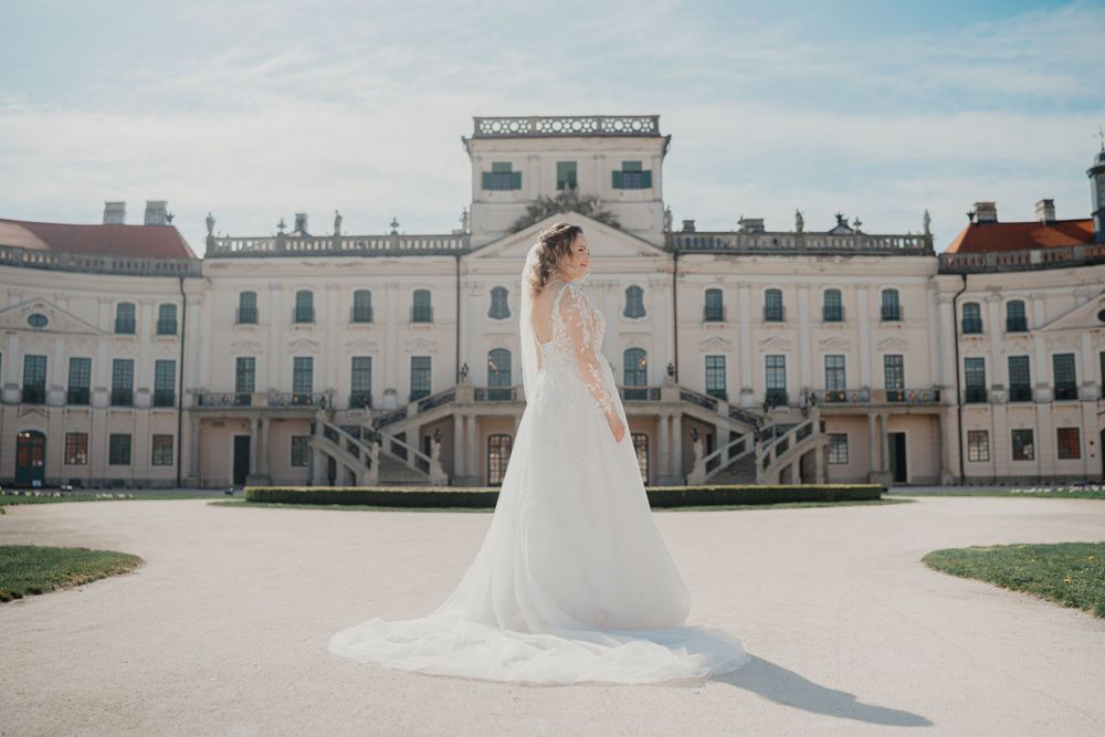 A white wedding gown against the backdrop of a grand historic palace with symmetrical architecture and manicured grounds.
