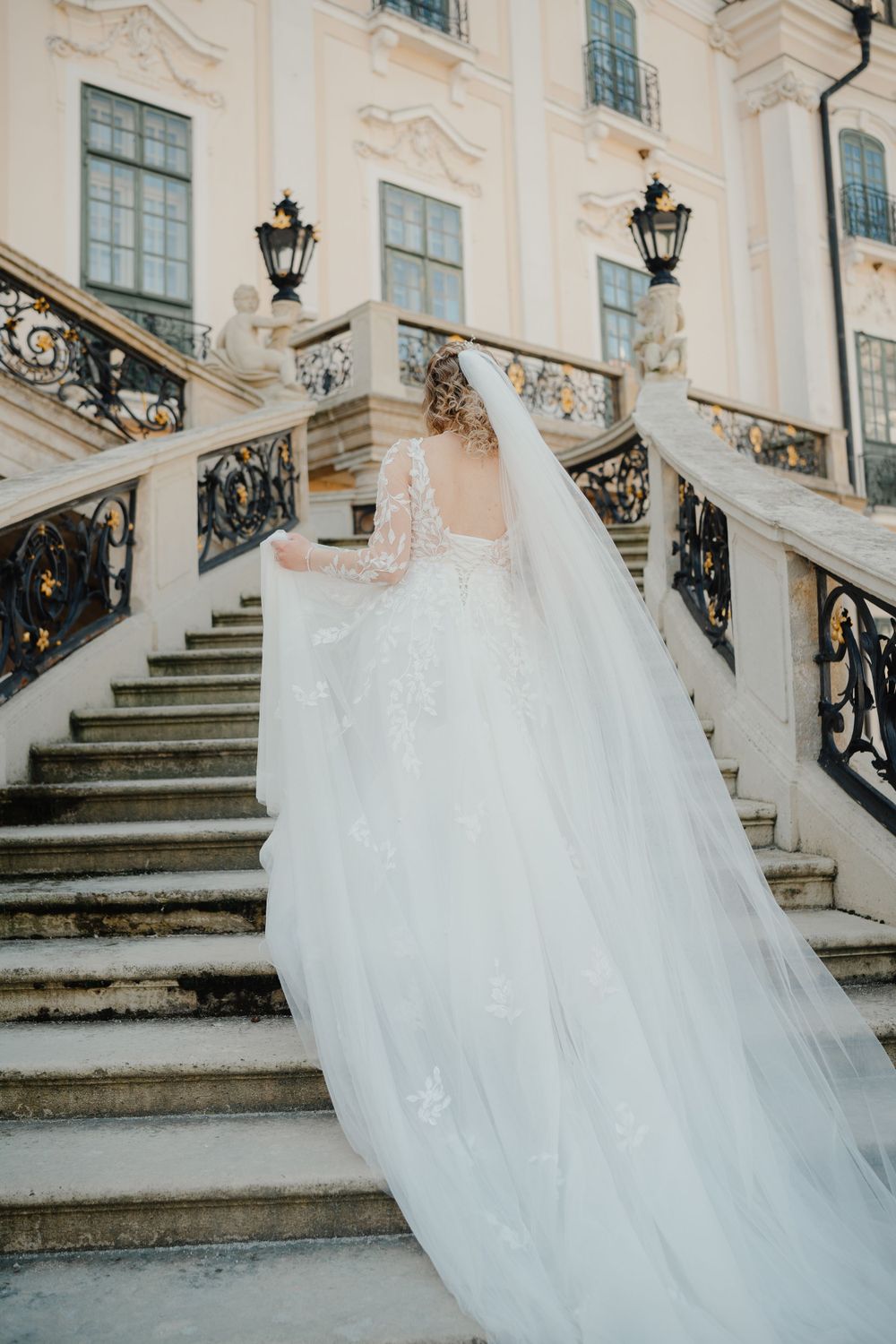 A flowing white wedding dress trailing behind on ornate marble steps of a classical building with decorative railings.
