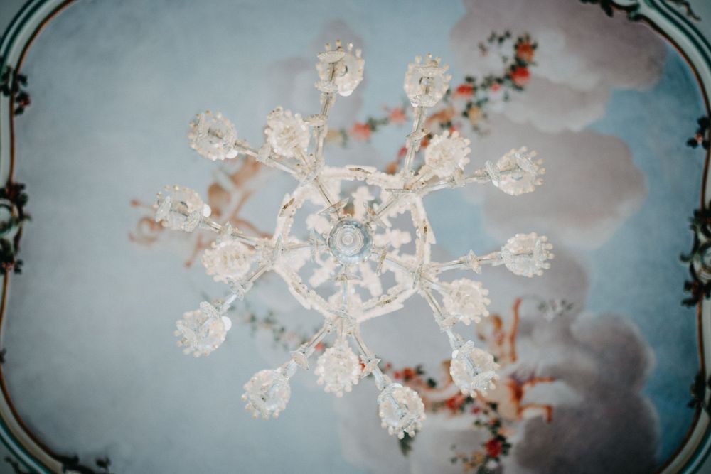 A crystal chandelier with delicate glass flowers and ornate details photographed from below against a soft blue ceiling.