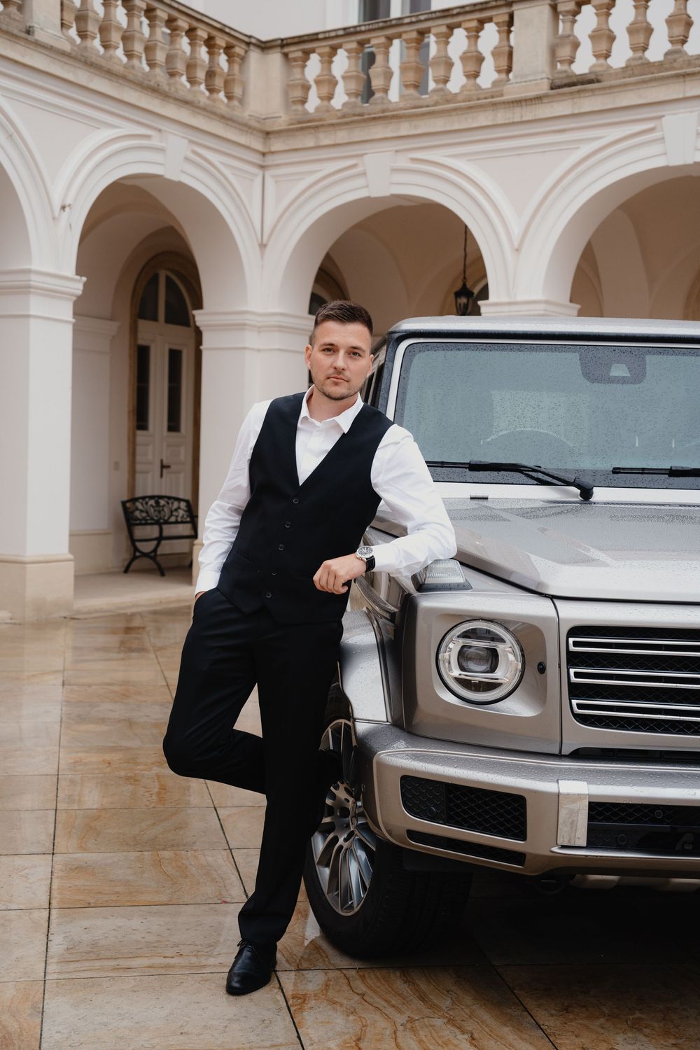A luxury Mercedes G-class SUV parked under elegant white archways with marble columns and balustrades.
