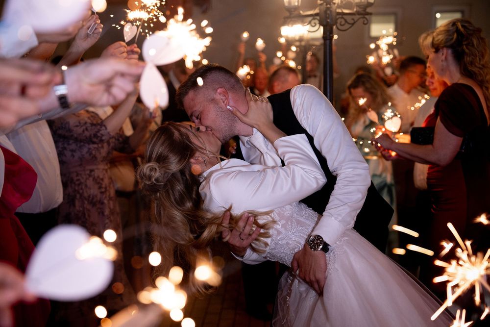 A romantic dance dip captured during a wedding reception with sparklers creating magical light trails in the background.