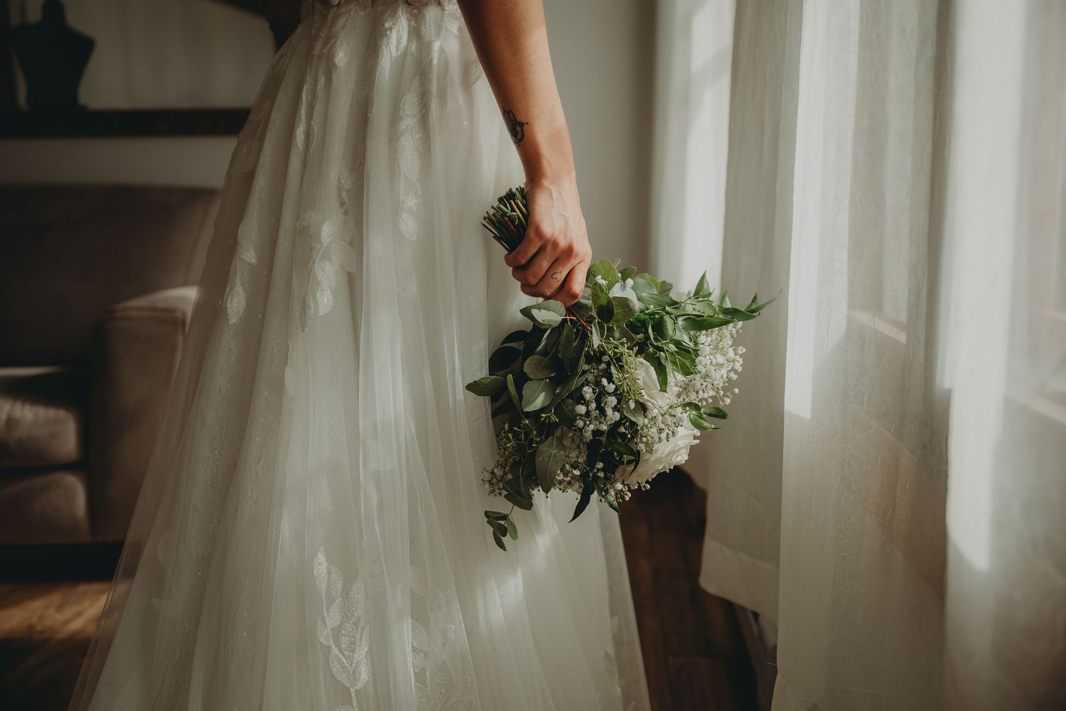 Detail shot of bride holding natural greenery and white floral bouquet against white dress.