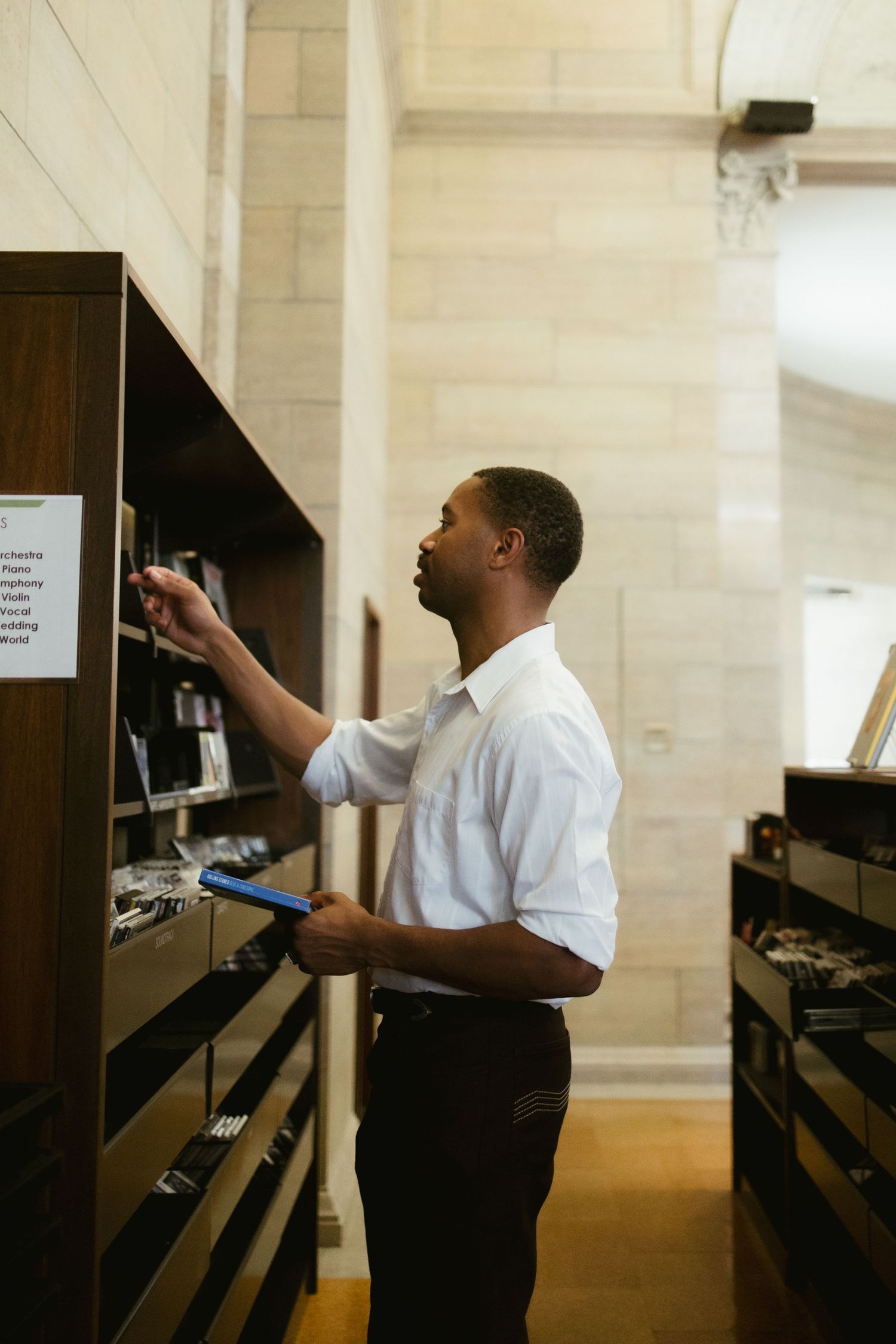 A person in business attire reaches for books on dark wooden library shelves.