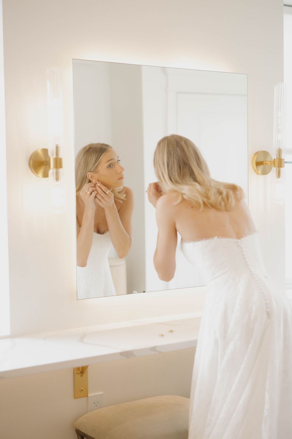 Multiple reflections in bathroom mirrors show a woman in white getting ready for a special occasion.