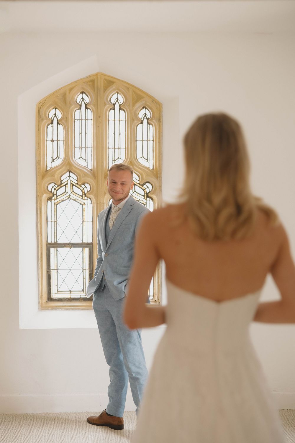 Wedding first look sequence with couple in white dress and blue suit in front of gothic window.